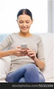 home, technology, communication and internet concept - woman sitting on the couch with smartphone at home