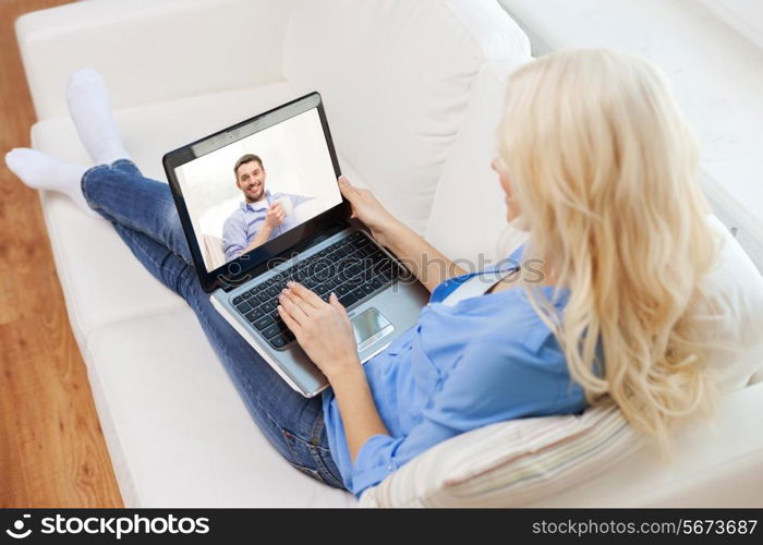 home, technology, communication and people concept - smiling woman sitting on couch and chatting with laptop computer at home