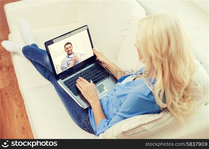 home, technology, communication and people concept - smiling woman sitting on couch and chatting with laptop computer at home