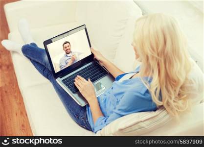 home, technology, communication and people concept - smiling woman sitting on couch and chatting with laptop computer at home