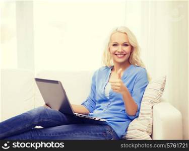 home, technology, gesture and internet concept - smiling woman sitting on the couch with laptop computer at home showing thumbs up