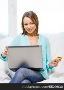 home, technology, online shopping and internet concept - smiling woman sitting on the couch with laptop computer at home