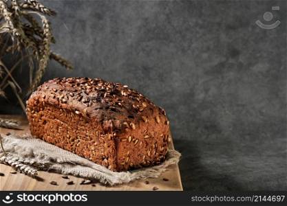Homebaked bread. Healthy wheat and rye bread with seeds on sacking, close-up with selective focus. Naturally fermented bread, healthy food. Loaf on gray background with space for text