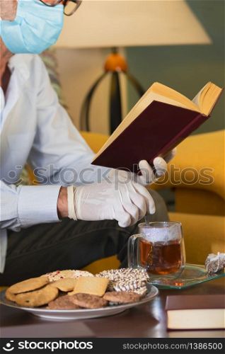 homebound man with medical gloves drinking a cup of tea and reading a book . prevention concept covid-19 concept. man with medical gloves drinking a cup of tea and reading a book