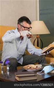 homebound man with medical gloves drinking a cup of tea and reading a book . prevention concept covid-19 concept. man with medical gloves drinking a cup of tea