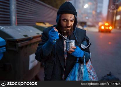 Homeless eating canned food on city street. Poverty is a social problem, homelessness and loneliness, alcoholism and drunk addiction, urban lonely. Homeless eating canned food on city street