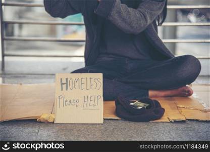 "Homeless people poverty beggar man asking for money job and hoping help in helpless dirty city sitting with sign of cardboard box said "Homeless Please Help" on board. Beggar in city concept."