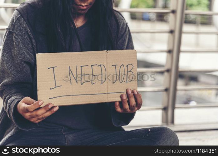 "Homeless people poverty beggar man asking for money job and hoping help in helpless dirty city sitting with sign of cardboard box said "I need job" on board. Beggar in city concept."