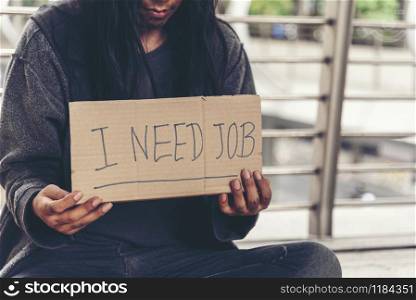 "Homeless people poverty beggar man asking for money job and hoping help in helpless dirty city sitting with sign of cardboard box said "I need job" on board. Beggar in city concept."