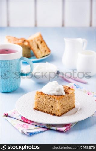 Homemade apple cake, slice with cream on plate, served for tea, selective focus