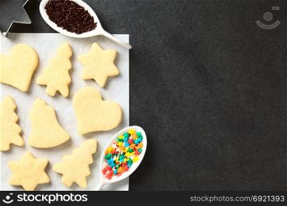 Homemade baked sugar cookies for Christmas with icing and sprinkles on the side, photographed overhead on slate. Homemade Sugar Cookies for Christmas
