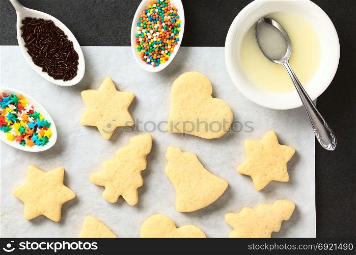 Homemade baked sugar cookies for Christmas with icing and sprinkles on the side, photographed overhead on slate. Homemade Sugar Cookies for Christmas