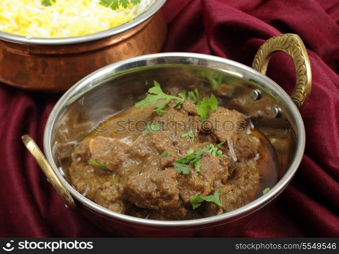 Homemade beef rogan josh in a balti dish with a bowl of yellow and white rice behind