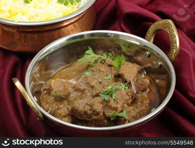 Homemade beef rogan josh in a balti dish with a bowl of yellow and white rice behind