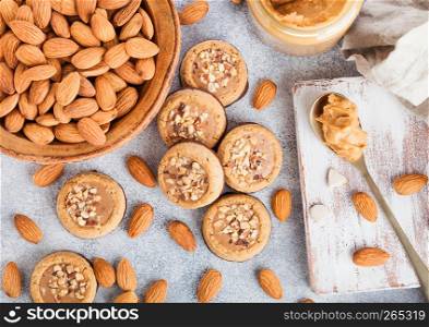 Homemade biscuit cookies with almond nuts and peanut butter on marble board on kitchen table background. Almonds in wooden bowl with jar and spoon of peanut butter.