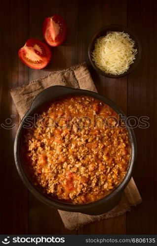 Homemade bolognese sauce made of fresh tomatoes, onion, carrot, garlic and mincemeat, served in rustic bowl, photographed overhead on dark wood with natural light (Selective Focus, Focus on the top of the sauce)