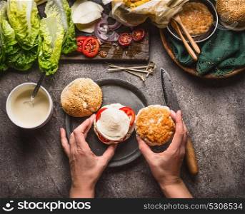 Homemade burger . Female woman hands making burger on kitchen table background with ingredients, top view