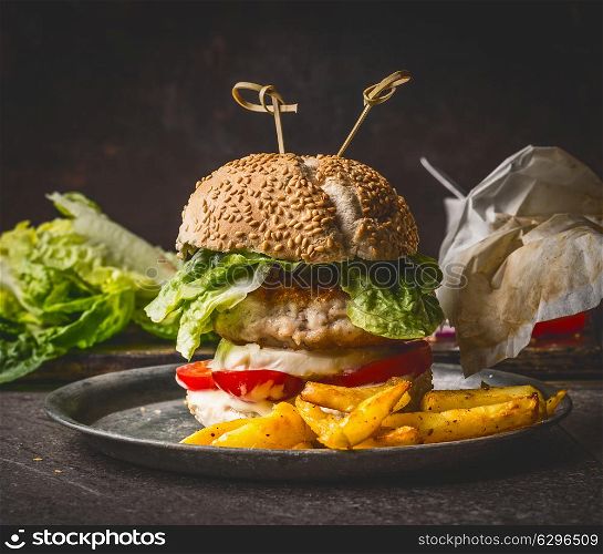 Homemade burger on dark rustic wooden background with French fries , front view, close up. Fast food and snack concept