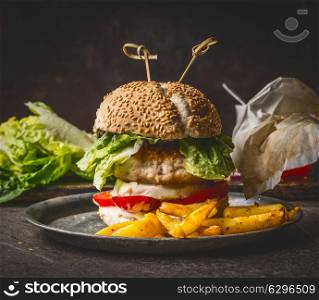 Homemade burger on dark rustic wooden background with French fries , front view, close up. Fast food and snack concept