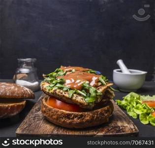 homemade burger with chicken in mustard sauce, arugula, tomatoes on a cutting board on wooden rustic background top view close up border,with text area
