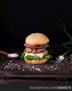 homemade burger with lettuce, cheese, onion and tomato on a rustic wooden board