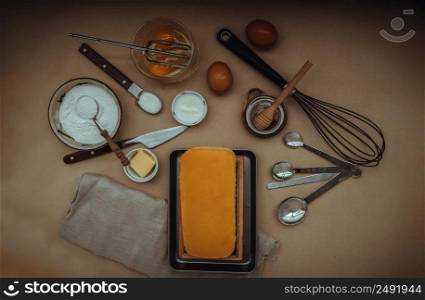 Homemade Butter cake or Pound cake with ingredients (eggs, flour, milk, butter with honey) and rolling pin, egg whisk on light brown table. Top view, Selective focus.