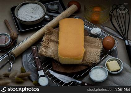 Homemade Butter cake or Pound cake with ingredients (eggs, flour, milk, butter with honey) and rolling pin, egg whisk on light brown table. Selective focus.