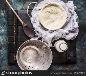 Homemade cheese making with cheesecloth , bottle of milk and wooden spoon on rustic background, top view