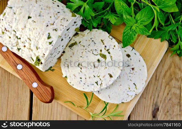 Homemade cheese with herbs and spices, cut into slices, knife, parsley, rosemary, basil, napkin on wooden board on top