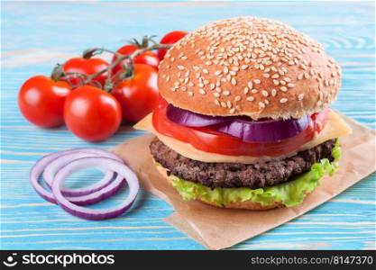 Homemade cheeseburger with beef patties, fresh salad, tomatoes and onion on seasame buns, served on blue wooden table.. Homemade cheeseburger on blue wooden surface.