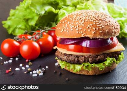 Homemade cheeseburger with beef patties, fresh salad, tomatoes and onion on seasame buns, served on black slate table.. Homemade cheeseburger on black slate surface.