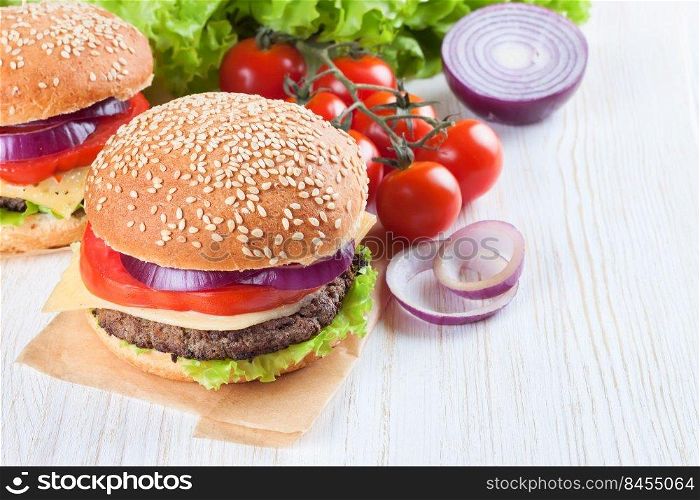 Homemade cheeseburger with beef patties, fresh salad, tomatoes and onion on seasame buns, served on white wooden table.. Homemade cheeseburger on white wooden surface.