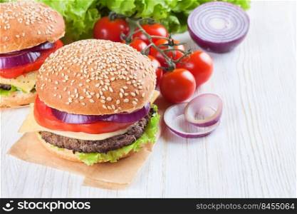Homemade cheeseburger with beef patties, fresh salad, tomatoes and onion on seasame buns, served on white wooden table.. Homemade cheeseburger on white wooden surface.