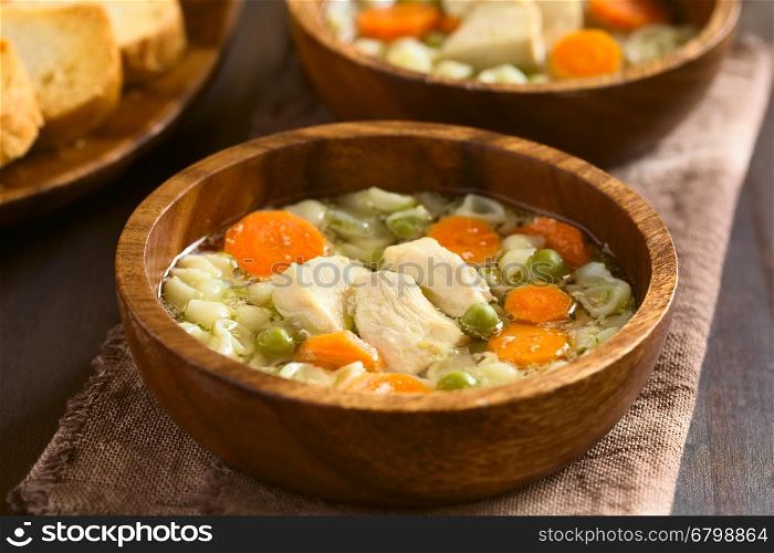 Homemade chicken soup with pea, carrot and small shell pasta in wooden bowls, photographed with natural light (Selective Focus, Focus on the front of the chicken in the first soup)