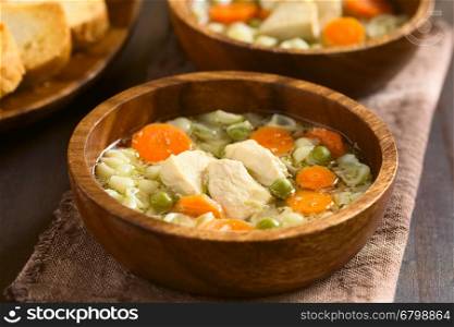 Homemade chicken soup with pea, carrot and small shell pasta in wooden bowls, photographed with natural light (Selective Focus, Focus on the front of the chicken in the first soup)