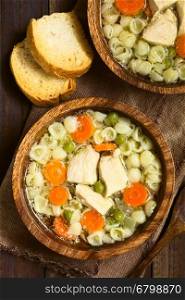 Homemade chicken soup with pea, carrot and small shell pasta in wooden bowls with toasted bread on the side, photographed overhead on dark wood with natural light (Selective Focus, Focus on the top of the soups)
