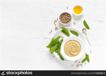 Homemade chickpea hummus served with green peas, healthy vegetarian food concept, top view