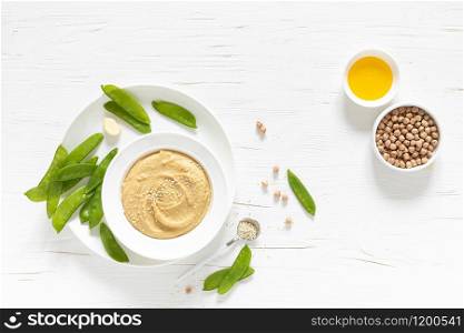 Homemade chickpea hummus served with green peas, healthy vegetarian food concept, top view