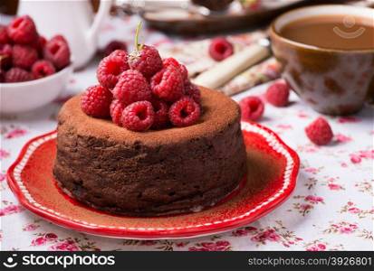 Homemade chocolate cake with raspberry on plate, cup of coffee and barries on side, selective focus