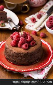 Homemade chocolate cake with raspberry on plate, cup of coffee and berries on side, selective focus