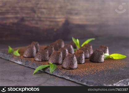 Homemade chocolate truffles with mint sprinkled with cocoa powder on slate. Focus on first truffle.