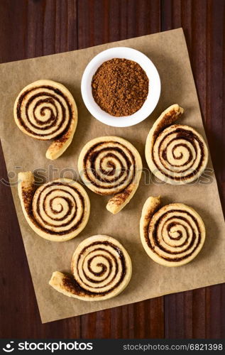 Homemade cocoa rolls or buns made of yeast dough and filled with sugar and cocoa powder, photographed overhead on dark wood with natural light