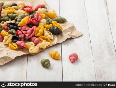 Homemade conchiglioni tricolore pasta in brown paper on white wooden background. Black, red and green pasta