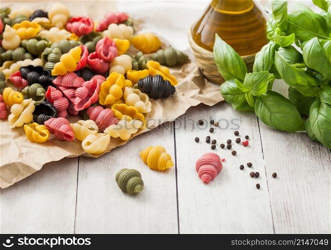 Homemade conchiglioni tricolore pasta in brown paper on white wooden background with basil and oil. Black, red and green pasta