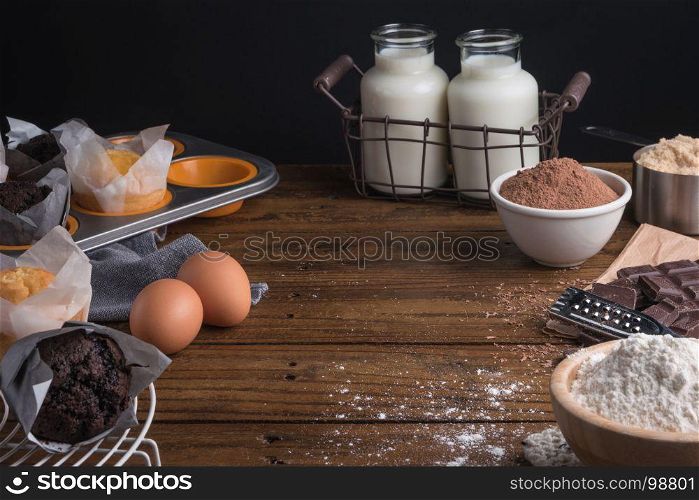 Homemade cooked muffins in a rustic setting with ingredients to cook on wooden table with copyspace.