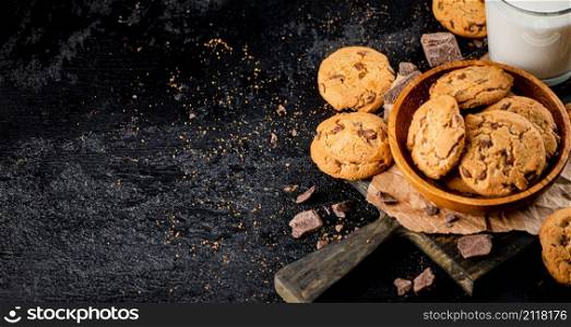 Homemade cookies with pieces of milk chocolate and a glass of milk. On a black background. High quality photo. Homemade cookies with pieces of milk chocolate and a glass of milk.