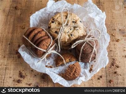 Homemade corded wholegrain cookies with oatmeal, linen and sesame seeds and traditional american cookies with chocolate chips on dark rustic wooden table . Healthy vegan food concept.. Various shortbread, oat cookies, chocolate chip biscuit.
