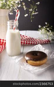 Homemade donut covered with chocolate glaze and glass of milk on white rustic wooden surface