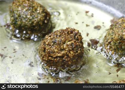 Homemade falafel mixture frying in oil. The balls comprise crushed soaked chickpeas, parsley and coriander leaves, coriander and cumin powder, chilli, paprika, salt and pepper.
