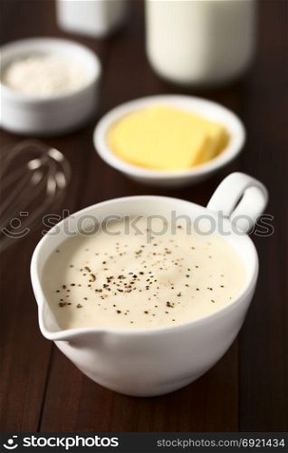 Homemade French Bechamel or White Sauce served in sauce boat with ingredients in the back (flour, butter, milk), photographed on dark wood with natural light (Selective Focus, Focus one third into the image). Bechamel or White Sauce